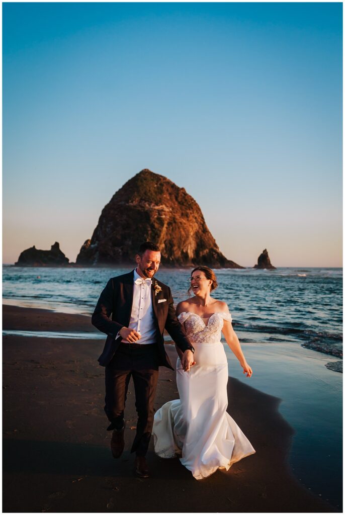 Newlyweds running in front of Haystack Rock on their Surfsand Resort Cannon Beach Micro Wedding on the Oregon Coast